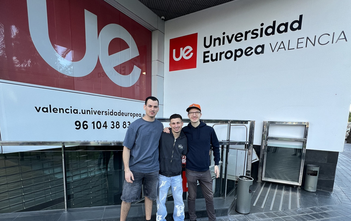 Drei junge Männer stehen Arm in Arm vor einer Wand mit der Aufschrift Universidad Europea Valencia
