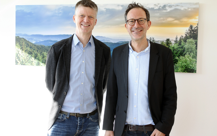 Zwei Männer stehen vor einem Schwarzwaldbild