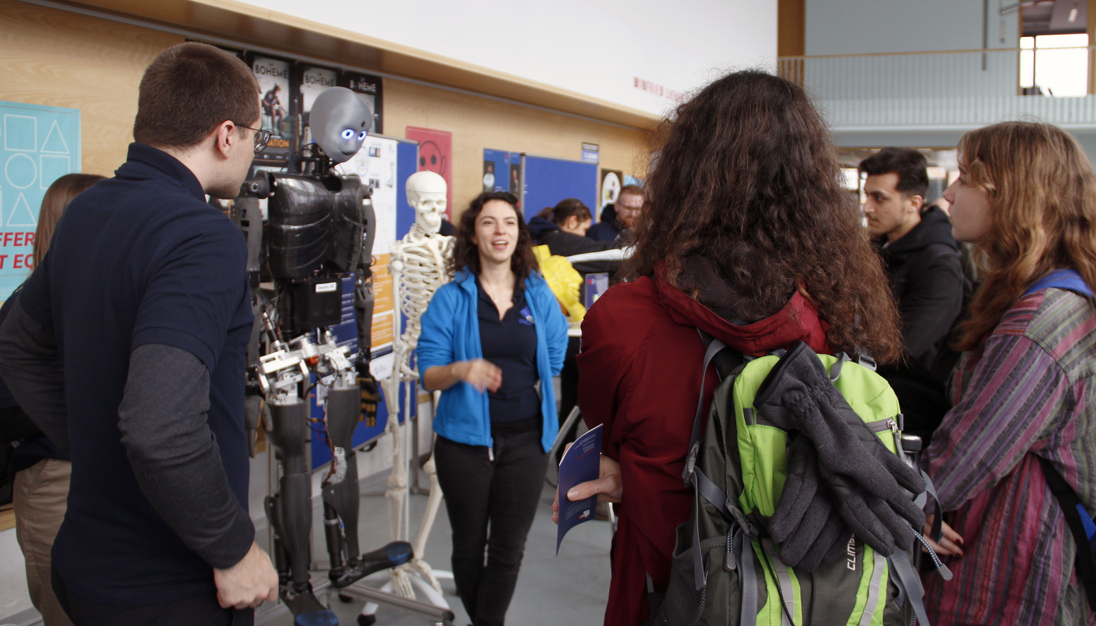 2023-11-23 Web-Meldung Studieninfotag Gespräch 2 Schülerinnen und Schüler umringen Roboter Sweaty und Skelett