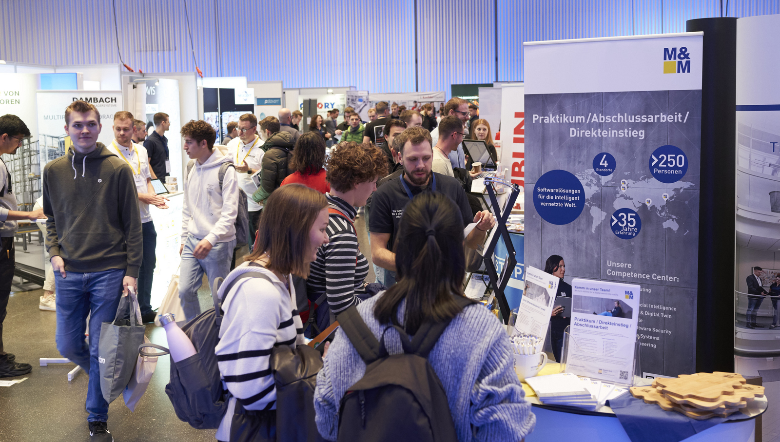 Blick in den großen Saal mit vielen Messeständen die umringt sind von Studierenden