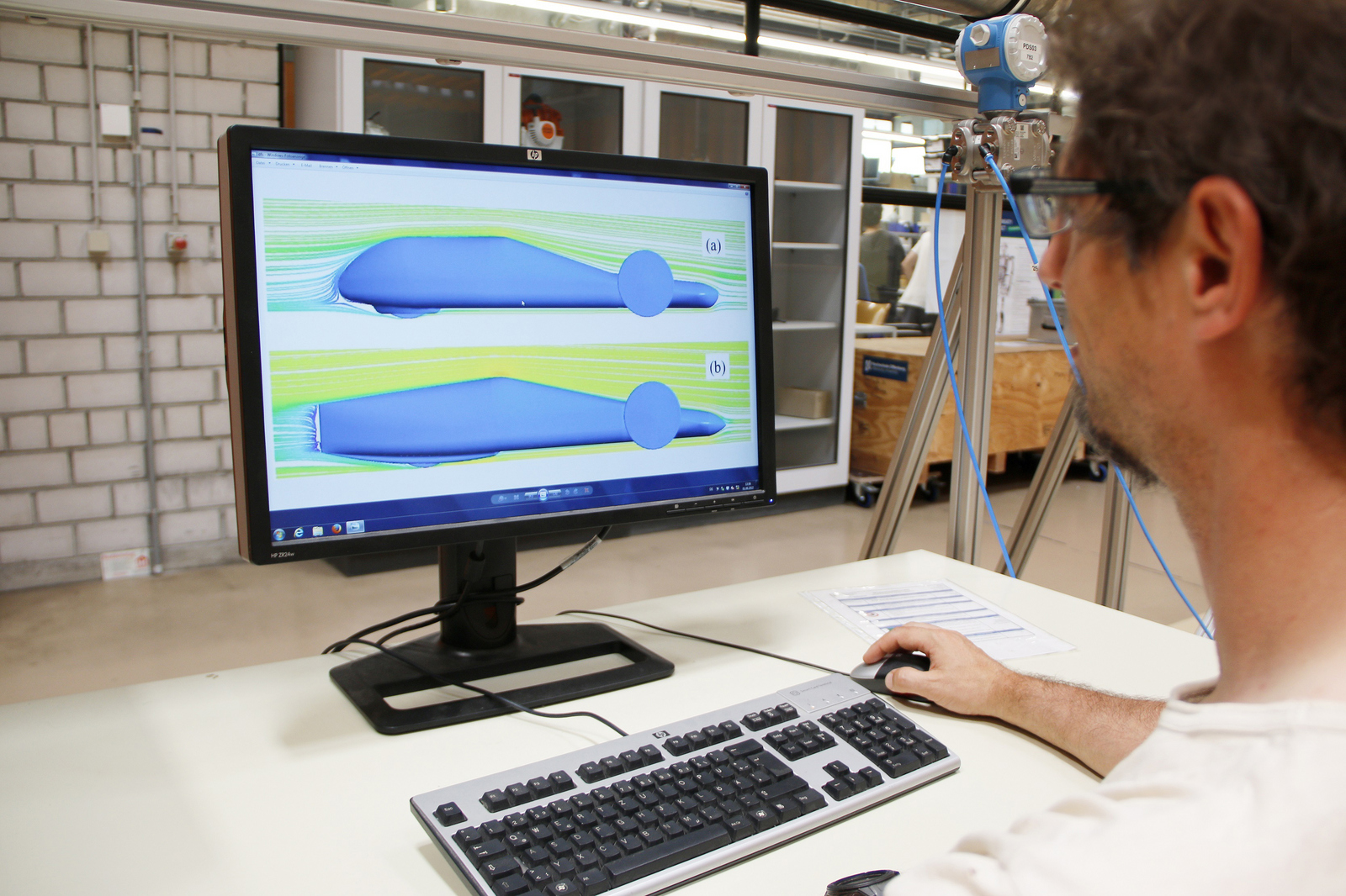 Ein Mann sitzt am PM, auf dem Bildschirm sind zwei unterschiedliche Fahrzeugdesigns und Strömungsverläufe grafisch dargestellt  