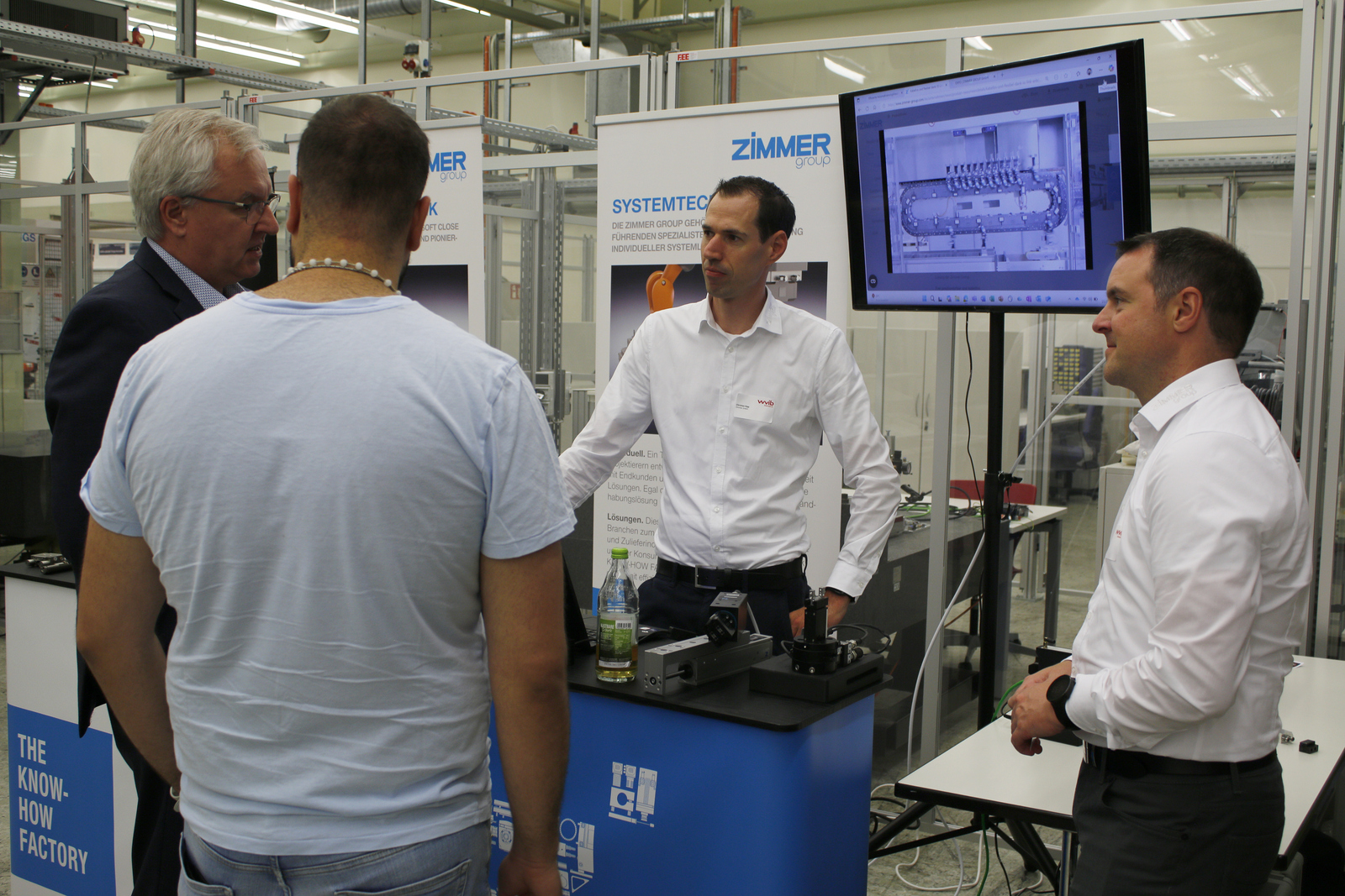2025-07-15 wvib Robotik Tag Ein Mann steht hinter einem Messestand und erklärt den Davorstehenden was auf dem Bildschirm rechts neben ihm zu sehen ist
