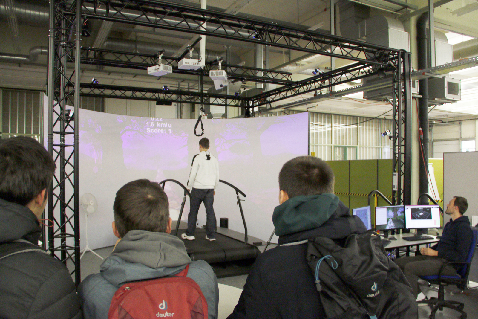 Junge läuft über die Laufband vor einem Videoscreen auf dem ein Weg zu sehen ist