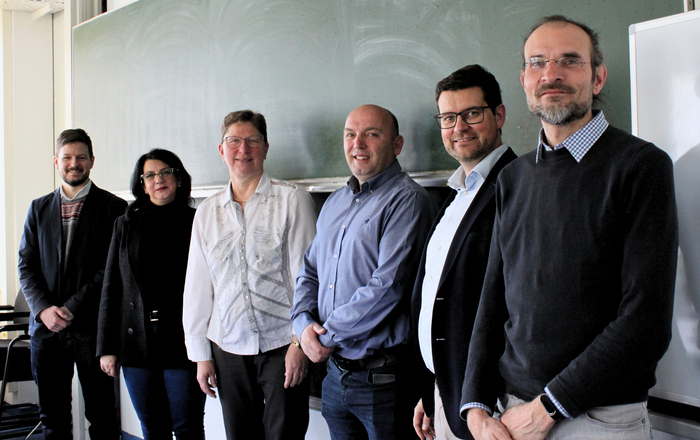 Sechs Männer und Frauen stehen vor einer Tafel