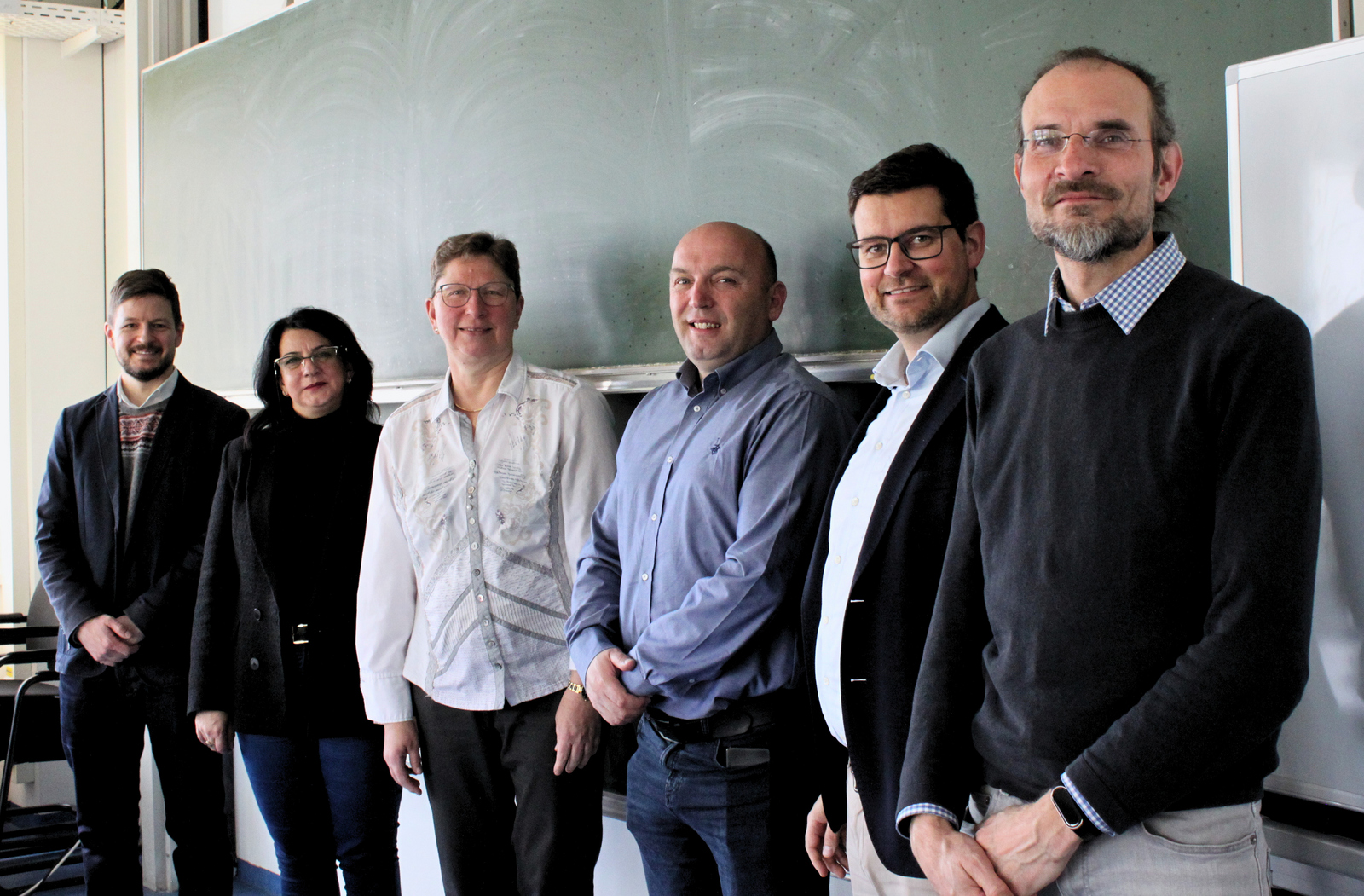 Sechs Männer und Frauen stehen vor einer Tafel