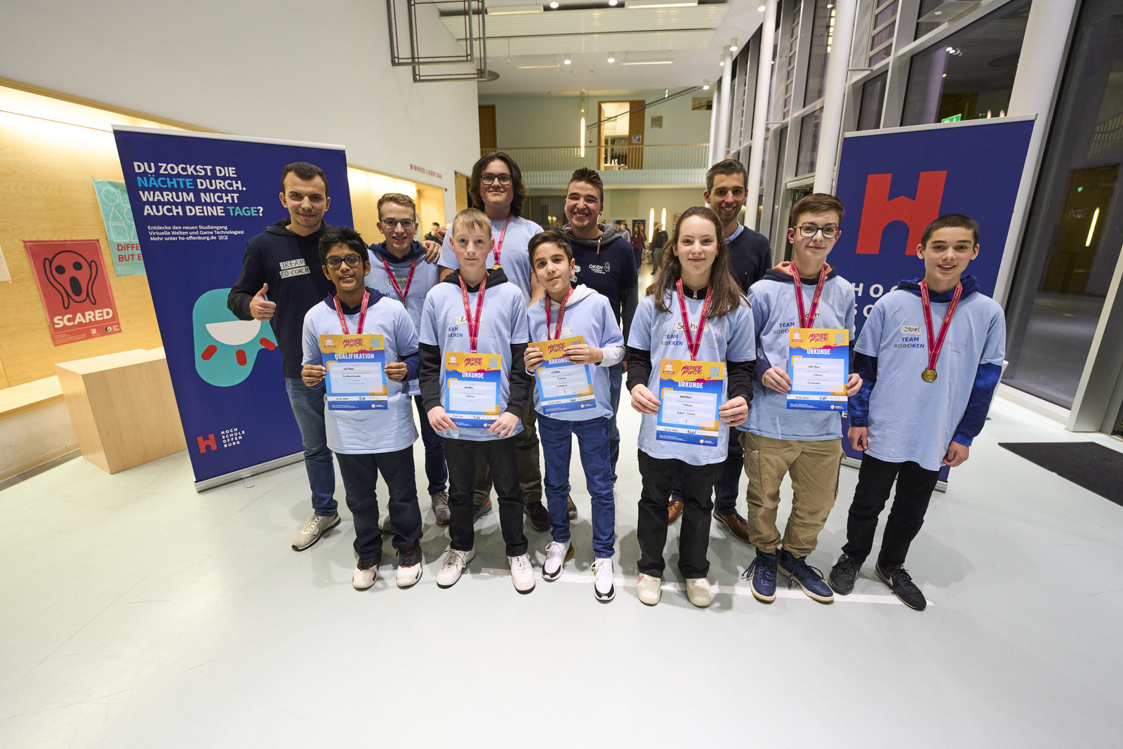 Team steht mit Urkunden im Foyer von Gebäude D