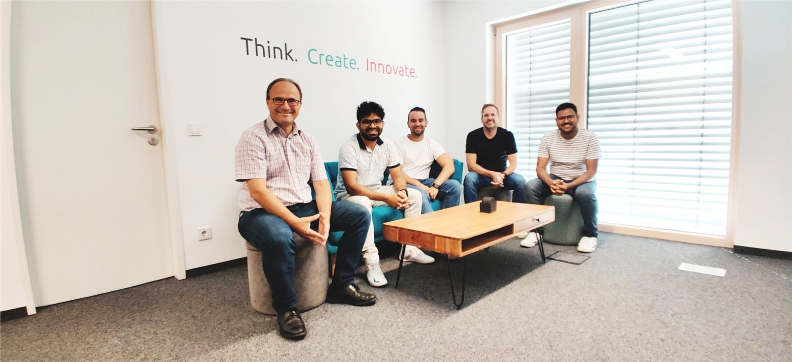 Die Projektbeteiligten sitzen unter der Überschrift Think. Create. an einem Couchtisch.