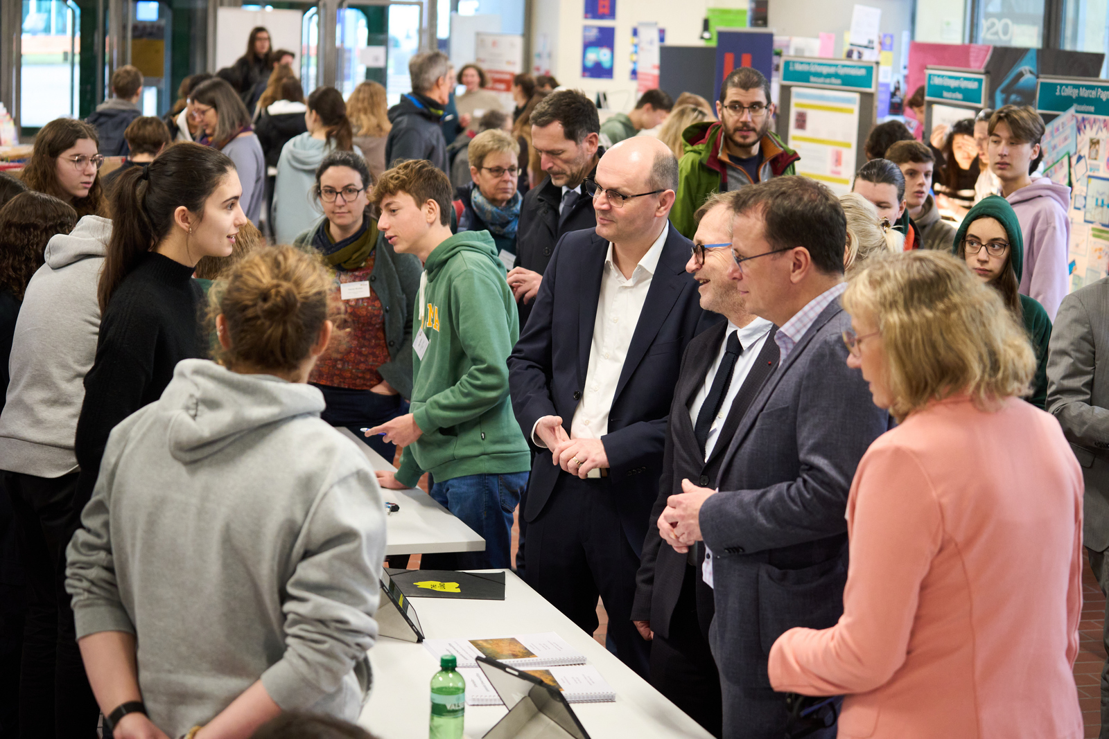 Trahasch, Faron, Schebesta stehen an einem Stand umringt von Schülern