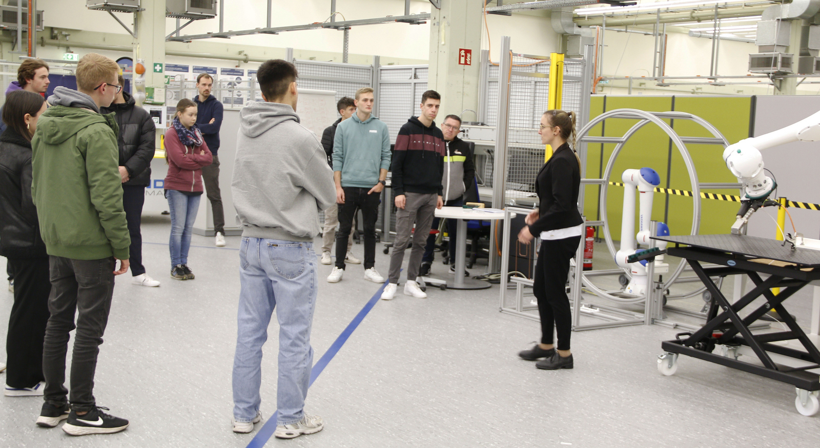 2023-11-23 Web-Meldung Studieninfotag Roboter Frau erklärt Schülerinnen und Schülern Roboter, der in einem Schwungrad hängt