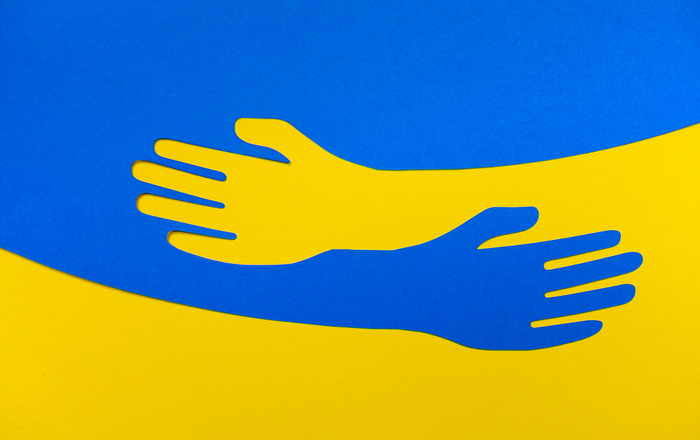 Die Grafik zeigt die ukrainische Flagge und auf dieser zwei umarmende gelbe und blaue Hände 