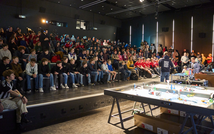 Zahlreiche Jugendliche sitzen in einem Hörsaal und warten, dass sie an die vorn stehenden Spieltische dürfen während ein Mann noch etwas erklärt