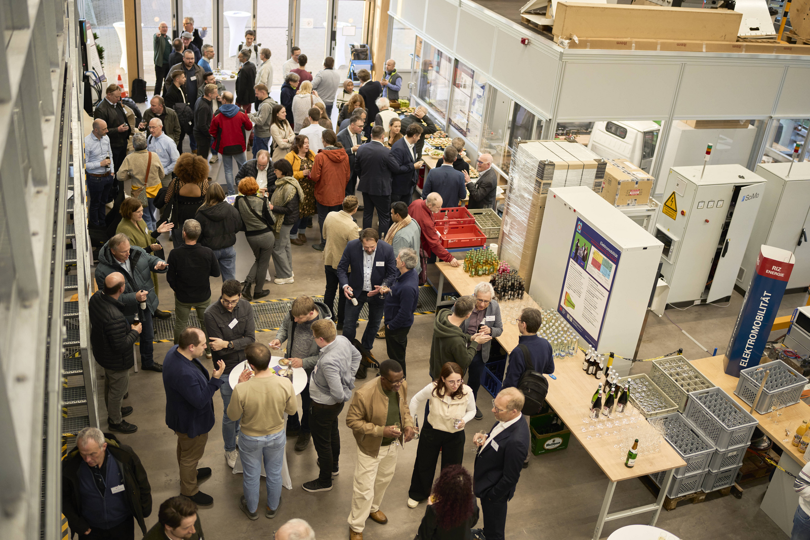 Blick von oben auf viele Menschen die in einem Technikum umherlaufen beziehungsweise sich an Stehtischen unterhalten