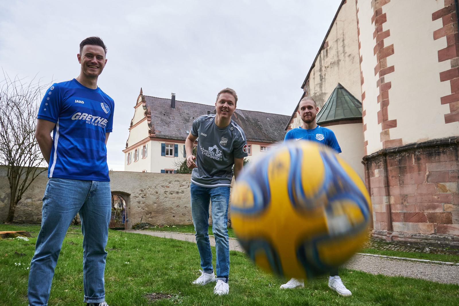 Tom Eisele, Pascal Oertel und Janik Zähringer (von links) in den Trikots ihrer jeweiligen Vereine und ein Ball der auf die Kamera zufliegt im Klostergarten in Gengenbach 