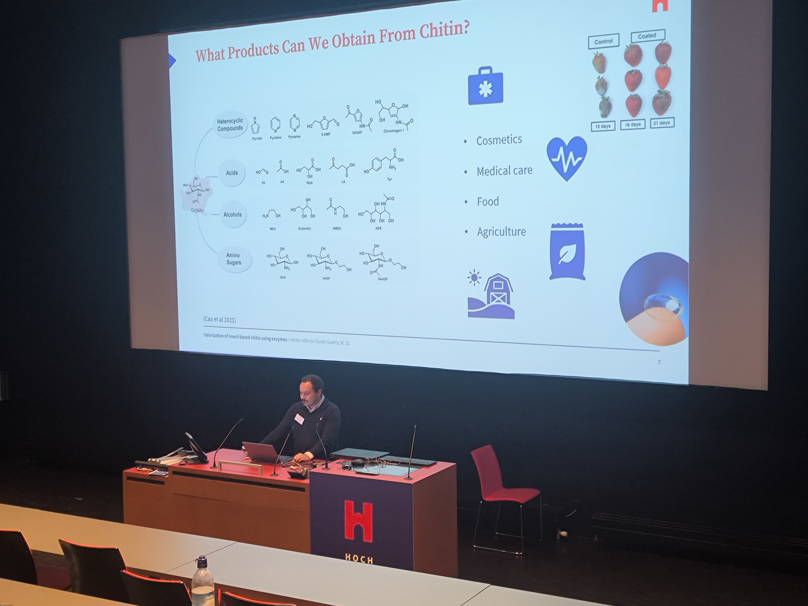 Ein Mann steht in einem Hörsaal vor einer Leinwand an einem Rednerpult
