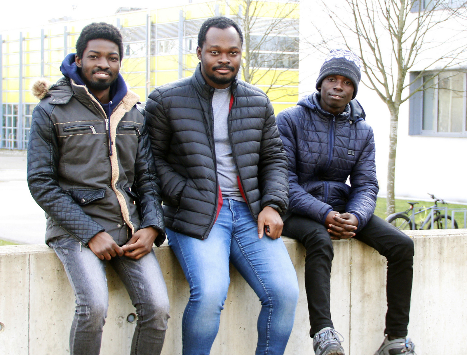 Seth Kotey, Nana Kwadwo Akrasi-Mensah und Robert Antwi von links auf einer Mauer auf dem Campus sitzend.