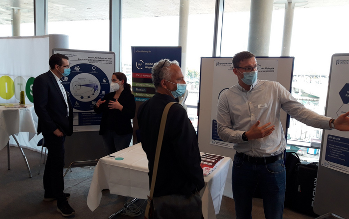 Zwei Doktoranden und zwei Messebesucher unterhalten sich am Stand der Hochschule Offenburg.