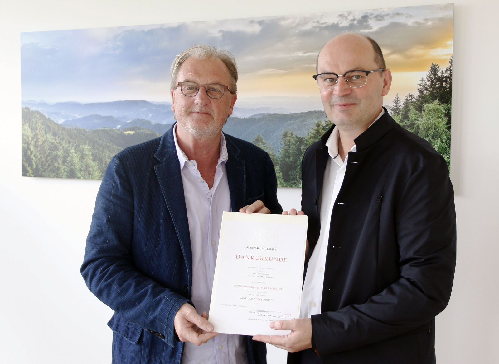 Heiner Behring (links) und Stephan Trahasch (rechts) stehen mit der Urkunde vor einem Schwarzwaldbild 