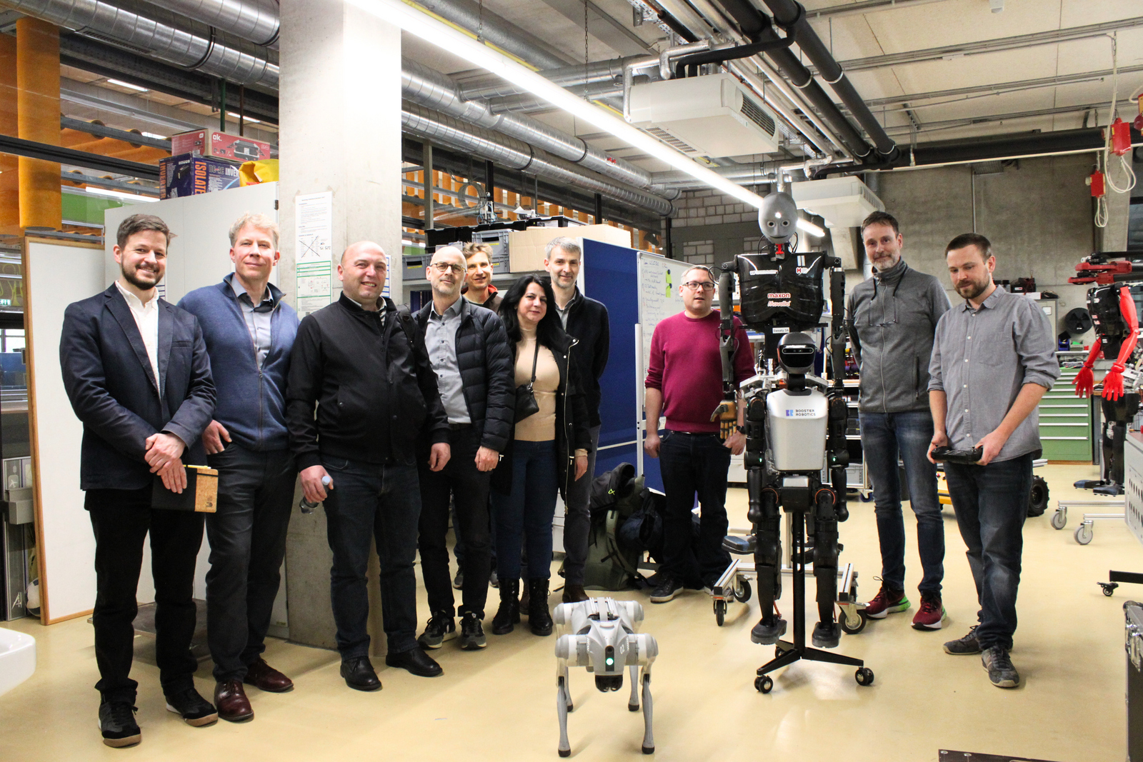 Männer und Frauen haben sich in einem Labor mit einem humanoiden Roboter und eine Roboterhund zum Gruppenfoto aufgestellt