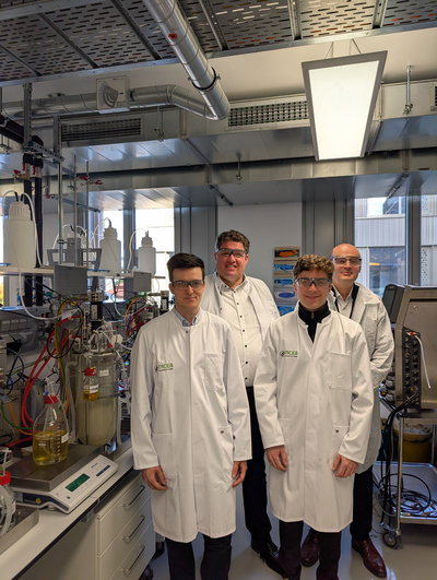 Vier Männer in weißen Kitteln und mit Schutzbrillen in einem Labor