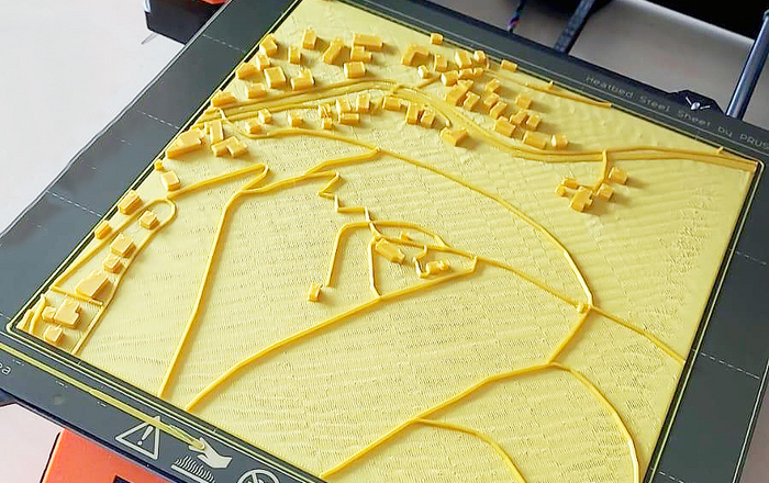 3D-Drucker auf dem ein haptisches Modell mit einer Dorf-/Stadtansicht steht