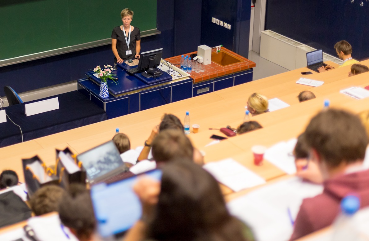 Eine Professorin steht in einem Hörsall vor Studierenden.