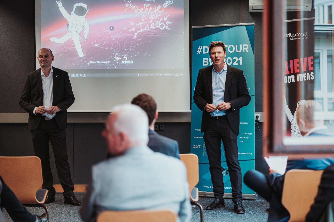 Prof. Dr. Stephan Trahasch (links) und Florian Appel (rechts) stehen vor den sitzenden Zuhörenden im Hintergrund ist eine Leinwand zu sehen.