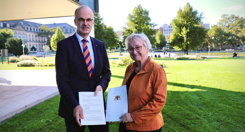 Ministerin Theresia Bauer (rechts) übergibt Prof. Dr. Volker Reuter (links), Vorsitzender der Rektorenkonferenz der HAW und des neu gegründeten Promotionsverbands, auf dem Rasen vor dem Ministerium die gerade unterzeichnete Rechtsverordnung zur Verleihung des Promotionsrechts. 