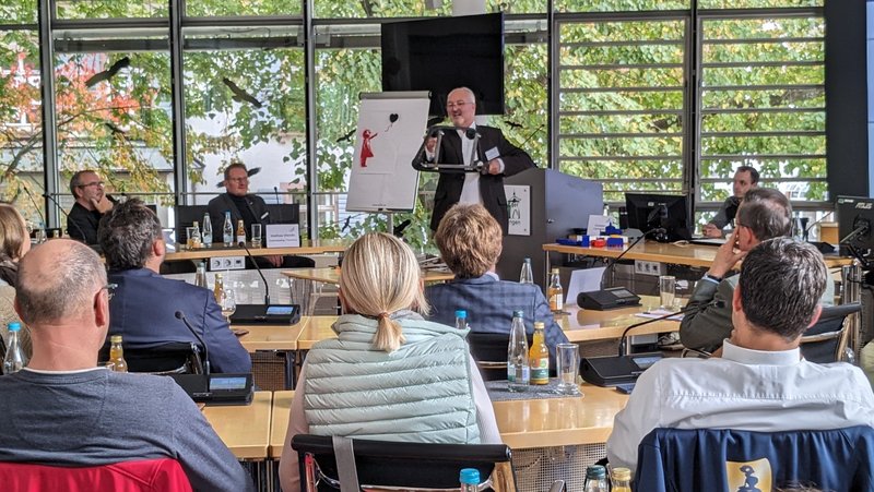 Günther Waibel steht vor einer Gruppe sitzender Menschen