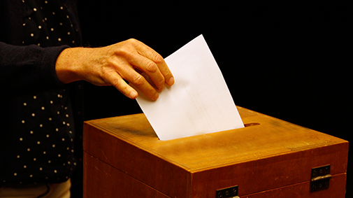 Hand steckt Wahlzettel in Wahlurne