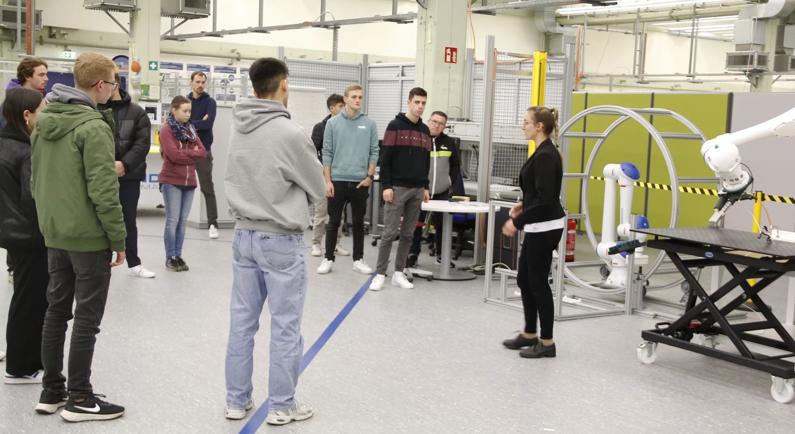 Eine Gruppe von Studenten in einem Labor mit Roboterarmen im Hintergrund